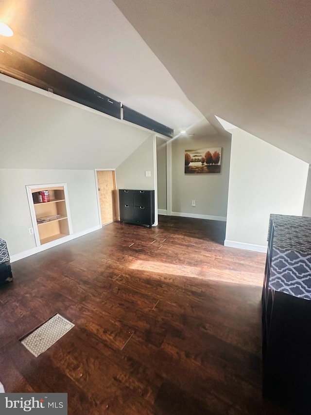 unfurnished living room with lofted ceiling with beams, built in shelves, dark wood finished floors, and baseboards