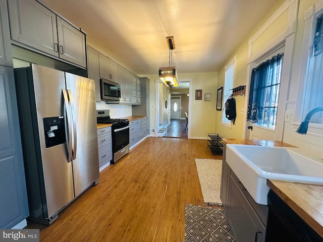 kitchen featuring stainless steel appliances, hanging light fixtures, gray cabinetry, and wooden counters