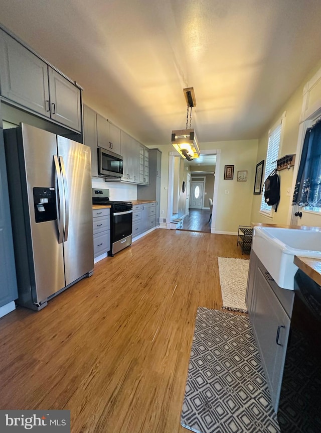 kitchen with decorative light fixtures, gray cabinets, light countertops, appliances with stainless steel finishes, and wood finished floors