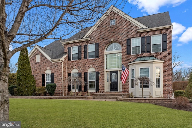 view of front facade featuring roof with shingles, a front lawn, and brick siding