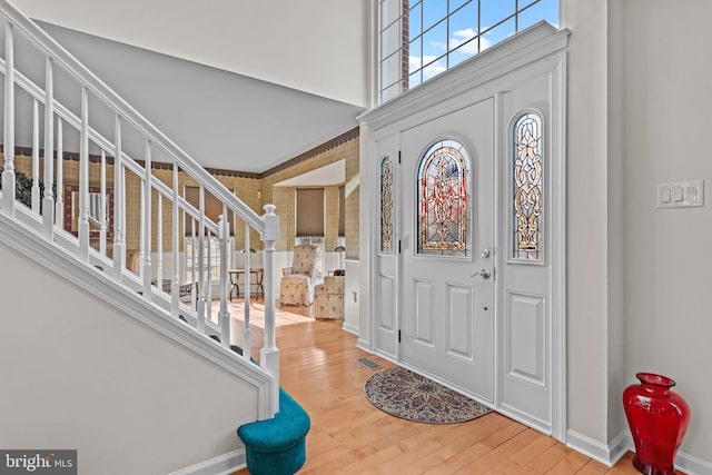 entryway with wood finished floors, visible vents, a towering ceiling, baseboards, and stairway