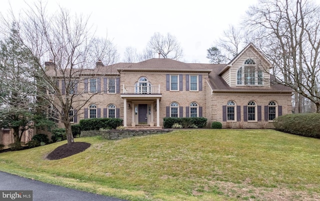 colonial inspired home featuring a front lawn, a balcony, and brick siding