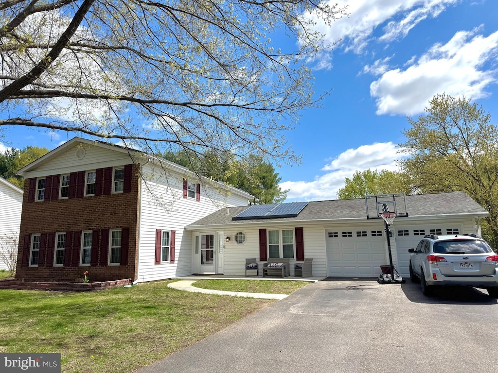 view of front of house featuring a garage, roof mounted solar panels, aphalt driveway, and a front yard
