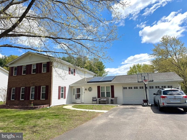 view of front of house featuring a garage, roof mounted solar panels, aphalt driveway, and a front yard