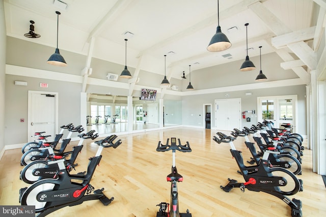 exercise room featuring baseboards, visible vents, wood finished floors, french doors, and high vaulted ceiling