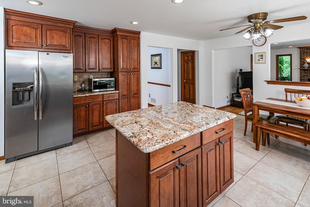 kitchen featuring appliances with stainless steel finishes, a ceiling fan, light stone countertops, decorative backsplash, and a center island