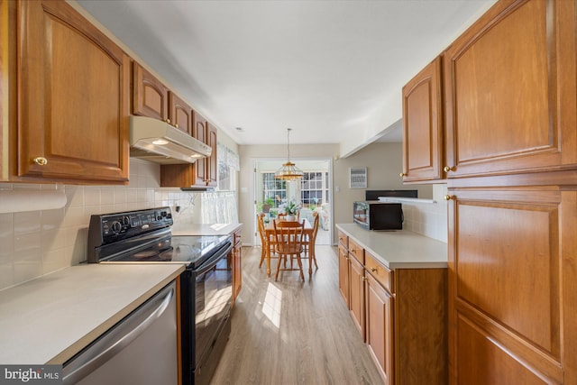 kitchen with brown cabinetry, under cabinet range hood, light countertops, light wood-type flooring, and black appliances