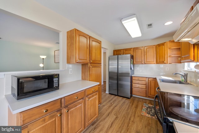 kitchen featuring visible vents, under cabinet range hood, light wood-type flooring, black appliances, and a sink