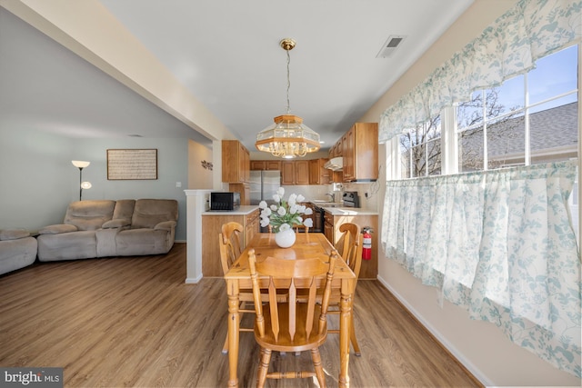 dining space with light wood-type flooring, visible vents, baseboards, and an inviting chandelier