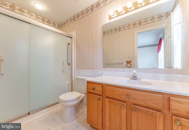 bathroom featuring toilet, wallpapered walls, wainscoting, a shower stall, and vanity