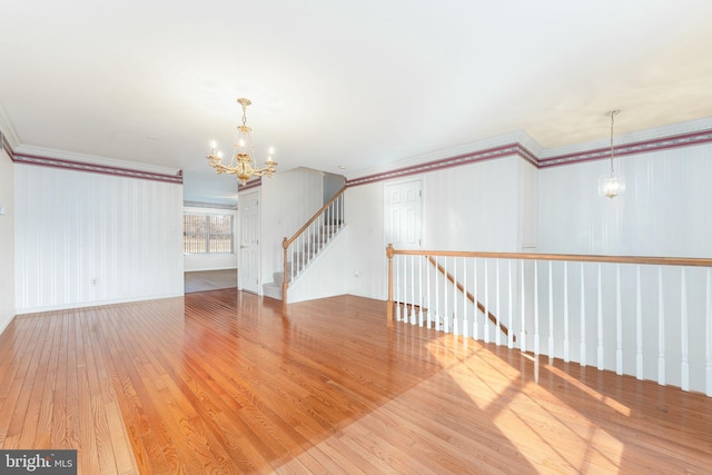 spare room featuring a chandelier, ornamental molding, stairs, and wood-type flooring