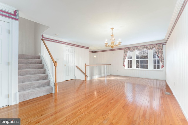 unfurnished living room with a notable chandelier, ornamental molding, stairs, and hardwood / wood-style floors