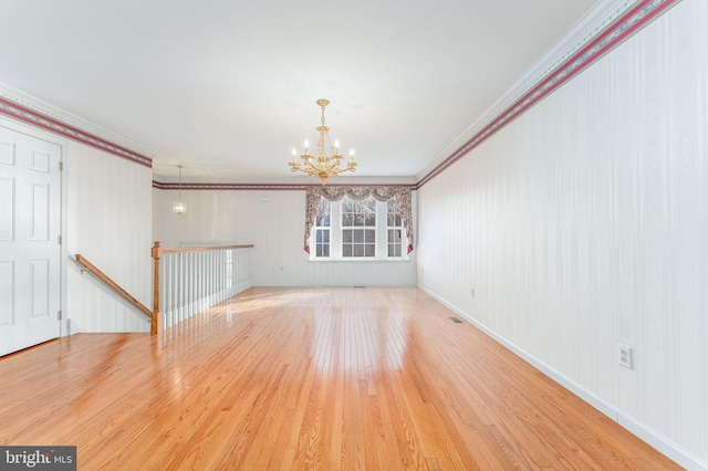 unfurnished room with visible vents, a notable chandelier, ornamental molding, hardwood / wood-style flooring, and baseboards