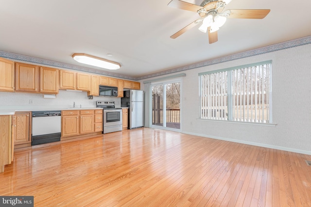 kitchen featuring baseboards, light countertops, light wood-style flooring, stainless steel appliances, and a sink