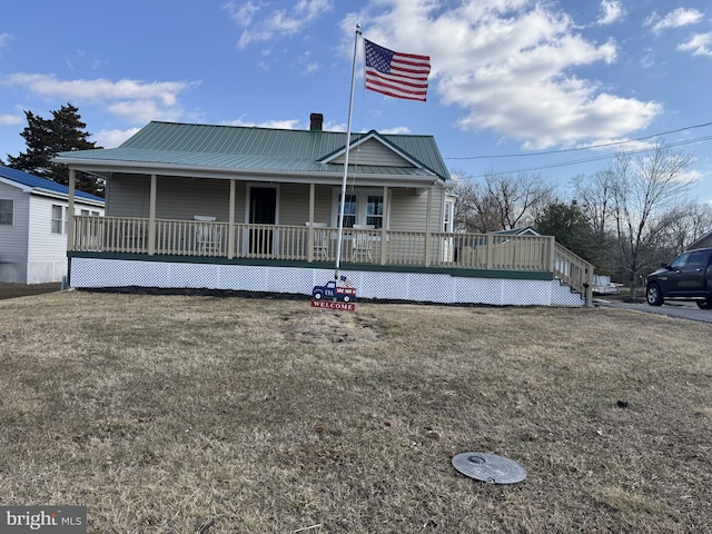 view of front of house with covered porch, metal roof, a chimney, and a front lawn