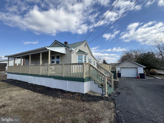 view of front facade with aphalt driveway, an outbuilding, covered porch, metal roof, and a garage