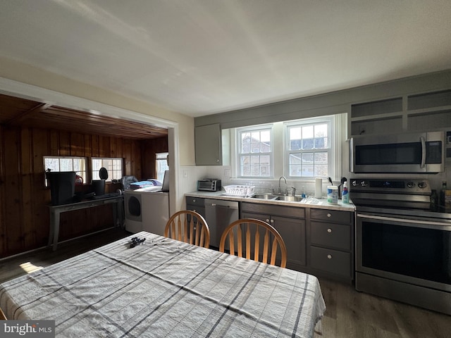 kitchen with wooden walls, appliances with stainless steel finishes, gray cabinets, light countertops, and a sink