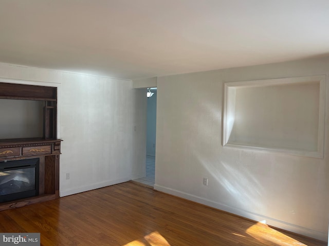 unfurnished living room with baseboards, wood finished floors, and a glass covered fireplace