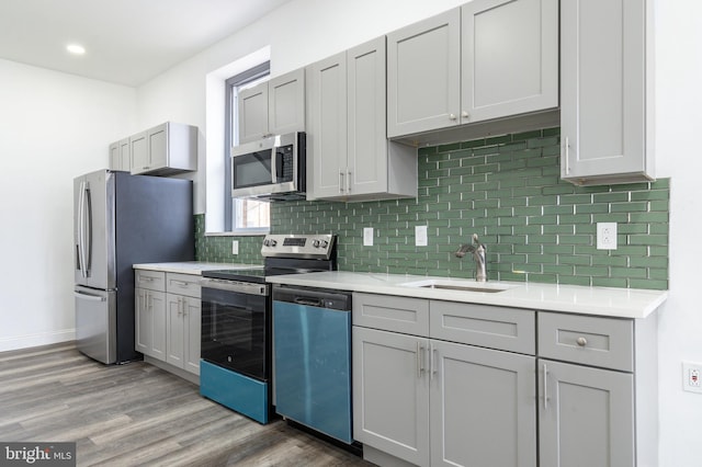 kitchen with stainless steel appliances, light countertops, gray cabinetry, a sink, and wood finished floors