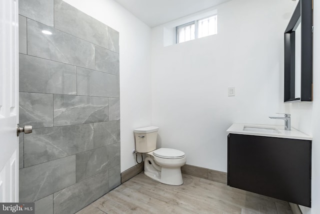 bathroom with toilet, wood finished floors, vanity, and baseboards