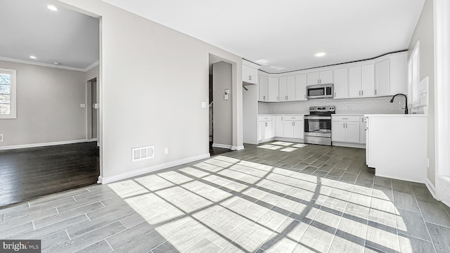 kitchen featuring decorative backsplash, stainless steel appliances, light countertops, wood finish floors, and white cabinetry