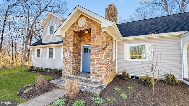 view of front of property featuring a front yard, stone siding, roof with shingles, and a chimney