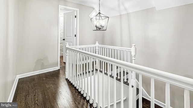 hall with a chandelier, wood finished floors, an upstairs landing, and baseboards