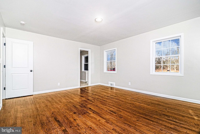 empty room featuring wood finished floors, visible vents, and baseboards