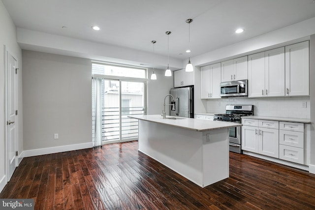 kitchen featuring a kitchen island with sink, stainless steel appliances, a sink, light countertops, and pendant lighting