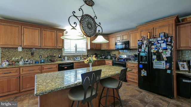 kitchen with a center island, hanging light fixtures, backsplash, light stone countertops, and black appliances