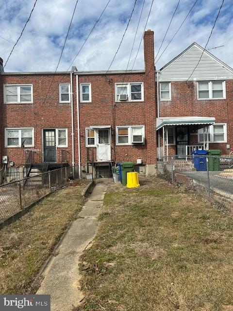 back of property with brick siding, a chimney, fence, and a lawn