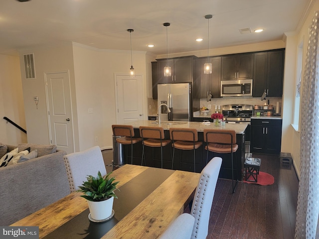 kitchen featuring a breakfast bar, decorative light fixtures, stainless steel appliances, visible vents, and a kitchen island with sink