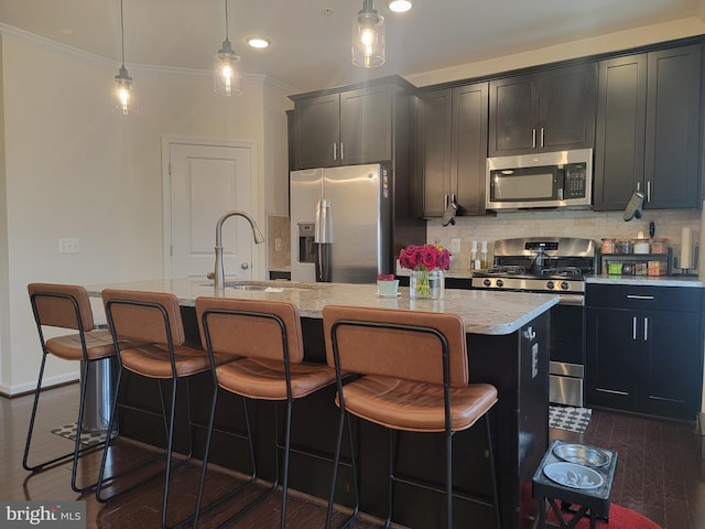 kitchen with appliances with stainless steel finishes, hanging light fixtures, an island with sink, and a kitchen bar