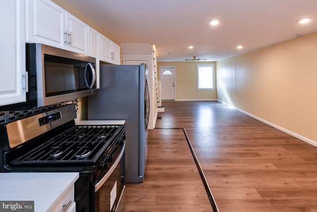 kitchen with light countertops, backsplash, appliances with stainless steel finishes, open floor plan, and white cabinetry