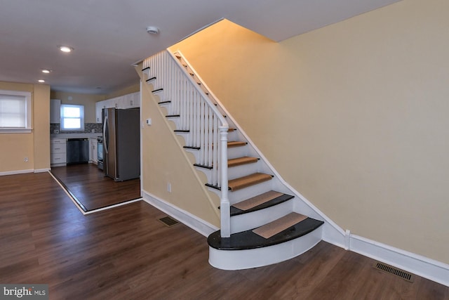 stairway featuring wood finished floors, visible vents, and baseboards