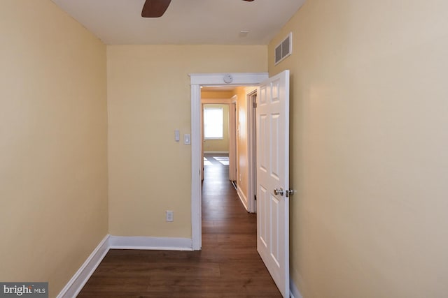 hall featuring visible vents, baseboards, and dark wood-type flooring