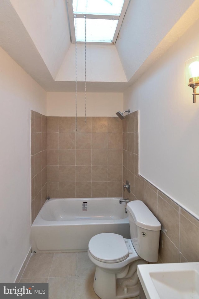 bathroom featuring vaulted ceiling with skylight, toilet, tile patterned floors, shower / washtub combination, and tile walls