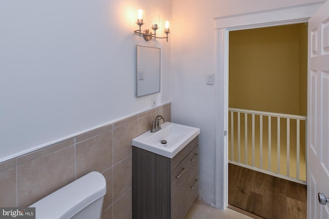 bathroom with toilet, a wainscoted wall, vanity, and tile walls