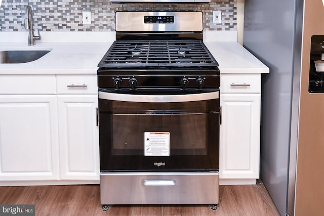 kitchen featuring appliances with stainless steel finishes, wood finished floors, light countertops, white cabinetry, and a sink