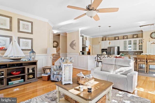 living area with a wainscoted wall, ornamental molding, visible vents, and light wood-style floors