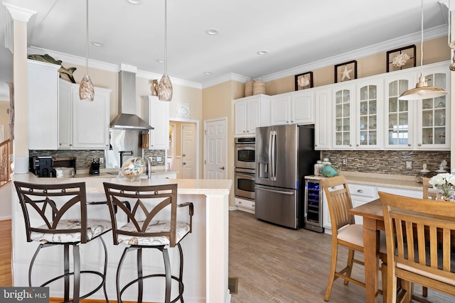 kitchen with wine cooler, appliances with stainless steel finishes, a breakfast bar area, a peninsula, and wall chimney range hood