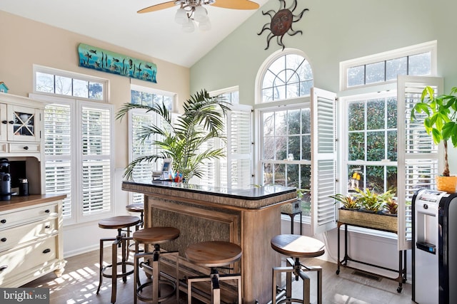 bar with ceiling fan, high vaulted ceiling, light wood-style flooring, visible vents, and baseboards