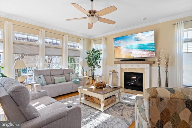 living room with a ceiling fan, a glass covered fireplace, crown molding, and wood finished floors