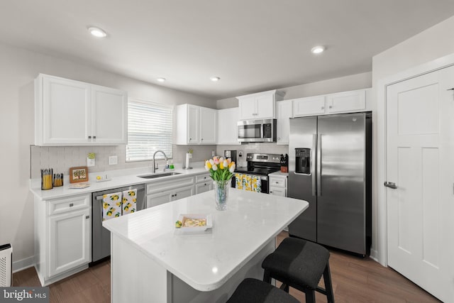 kitchen with stainless steel appliances, white cabinetry, a kitchen island, a sink, and a kitchen breakfast bar