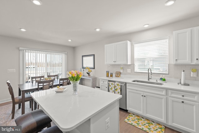 kitchen featuring a center island, light countertops, stainless steel dishwasher, white cabinetry, and a sink