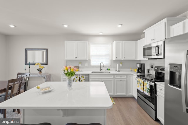 kitchen featuring white cabinets, stainless steel appliances, light wood-type flooring, a kitchen bar, and a sink