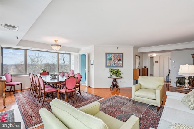 living area featuring visible vents, baseboards, light wood-style flooring, and crown molding