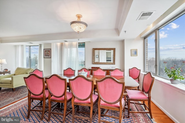 dining room with wood finished floors, visible vents, baseboards, ornamental molding, and a raised ceiling