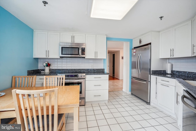 kitchen featuring light tile patterned floors, stainless steel appliances, tasteful backsplash, white cabinets, and dark stone counters