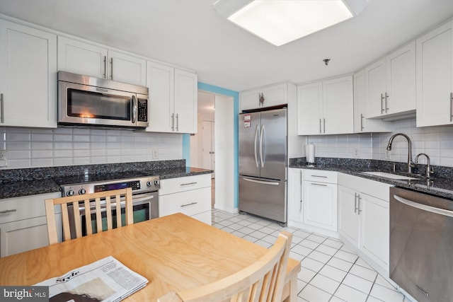 kitchen featuring tasteful backsplash, white cabinets, appliances with stainless steel finishes, a sink, and light tile patterned flooring